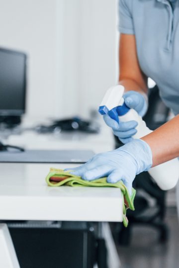 Close up view of woman in protective gloves that cleaning tables in the office